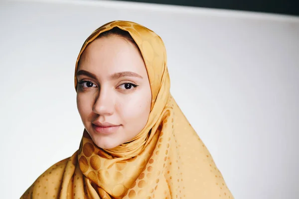 Mulher muçulmana em um lenço de cabeça olha calmamente para a câmera. luz de fundo — Fotografia de Stock