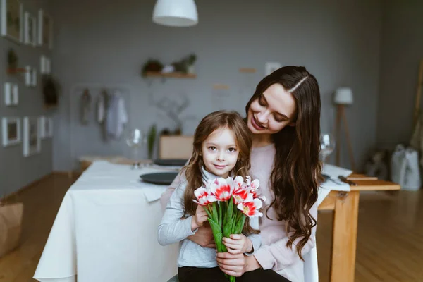 Tochter sitzt in den Armen ihrer Mutter und hält einen Strauß Tulpen in der Hand — Stockfoto