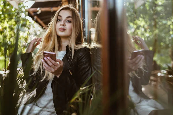 Beautiful blonde proudly looks at the camera, holds a phone in her hand, on the street near the cafe — Stock Photo, Image