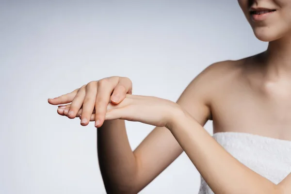 En el marco, hermosas manos femeninas con la piel delicada hacen movimientos como si frotando crema, la barbilla de las niñas y el hombro desnudo son visibles. fondo gris —  Fotos de Stock