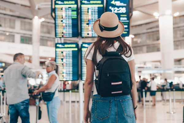 Tourist with a backpack and a hat at the airport looks at the arrival board — Stock Photo, Image