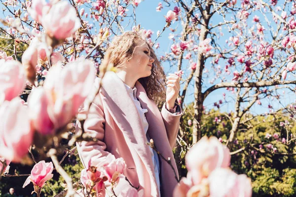 Luxurious pink magnolia flowers on the trees and among them is a girl in a pink coat — Stock Photo, Image