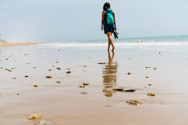 La spiaggia deserta, l'oceano si è allontanato e nella sabbia si possono vedere le tracce di una figura solitaria di una ragazza scalza che cammina lungo la riva con uno zaino dietro — Foto Stock