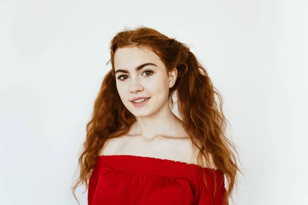 A young beautiful schoolgirl with ponytails of luxurious red hair, a magnificent white-toothed smile and an expressive look, is standing in a light-colored studio — Stock Photo, Image