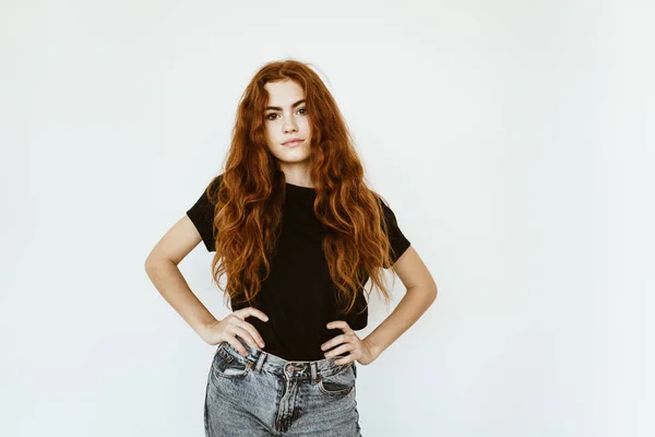 Uma menina adolescente encolheu o cabelo encaracolado vermelho longo e grosso sobre seus ombros e akimbo está de pé na frente da câmera — Fotografia de Stock