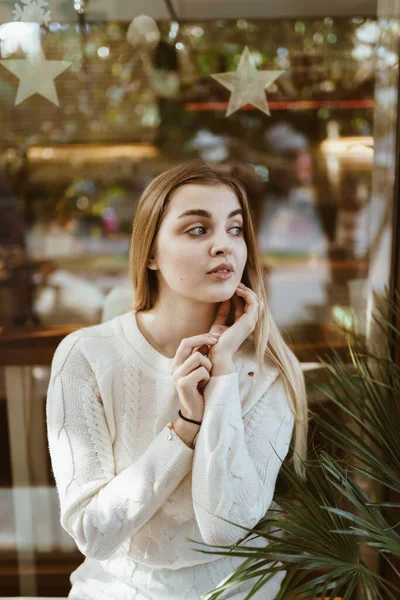Långhårig blondin sitter på ett café och tittar förväntansfullt in i fjärran fingrar hennes örsnibb — Stockfoto