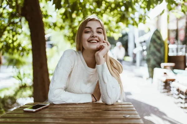 Bella bionda gioiosa sorride amabilmente seduta a un tavolo di un caffè di strada — Foto Stock