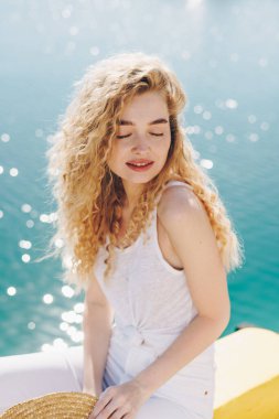 Kıvırcık sarışın, parlak bir denize karşı gözlerini kapayan güneşi sever.