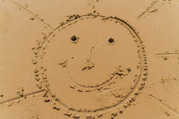 Disegnando sulla sabbia della spiaggia raffigura un sole stilizzato con un sorriso e occhi — Foto Stock