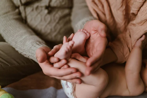 Las palmas del padre y la madre abrazan suavemente los pequeños pies del bebé acostado, sus brazos tocan el codo de la madre — Foto de Stock