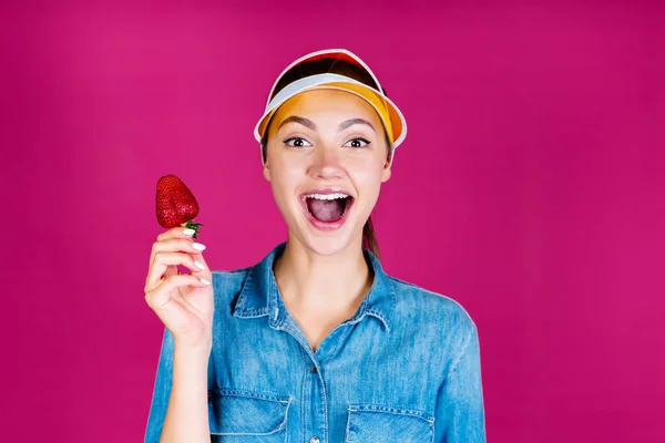 Ah! dice la ragazza nella visiera che tiene una fragola tra le mani. sfondo rosa — Foto Stock