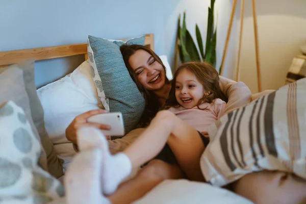 Mama i córka rano w łóżku śmieją się i robią sobie selfie — Zdjęcie stockowe