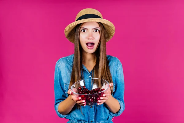 Sguardo stupito e bocca aperta da inaspettatezza in una ragazza con un cappello che tiene in mano un vaso di ciliegie — Foto Stock