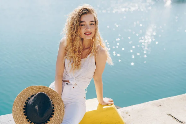 Lockigt blond kärleksfullt leende sitter på en pir på bakgrunden av glittrande vatten — Stockfoto