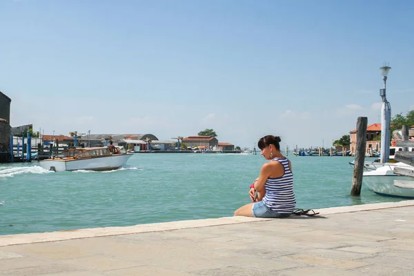 Summer. Italy. Burano. A girl sits on the embankment in the port