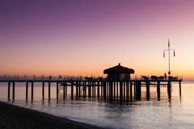 Bungalov pier üzerine güneş ışığı ile sular altında olduğunu. Leylak şafak gökten.