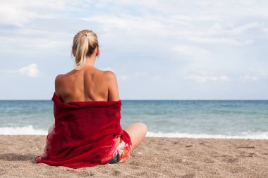 Sıcak açık güneşli yaz günü. Onun omuz ve kot şort bard bir kızla kamera arkası üzgün kıyıda oturur ve denizde görünüyor