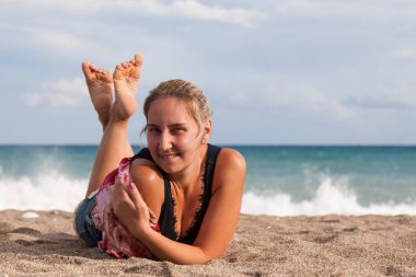 Sıcak açık güneşli yaz günü. Bir kız bir mavi T-shirt ve kot şort kamera karşı karşıya üzgün sahilde yatıyor