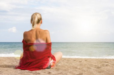 Sıcak açık güneşli yaz günü. Onun omuz ve kot şort bard bir kızla kamera arkası üzgün kıyıda oturur ve denizde görünüyor