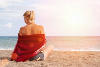 Sıcak açık güneşli yaz günü. Onun omuz ve kot şort bard bir kızla kamera arkası üzgün kıyıda oturur ve denizde görünüyor