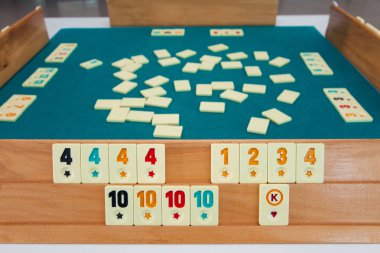 Türk masa oyunu Okey (Rummikub). Yeşil kumaş ve cipsli bir masa. Oyuncuların elleri.