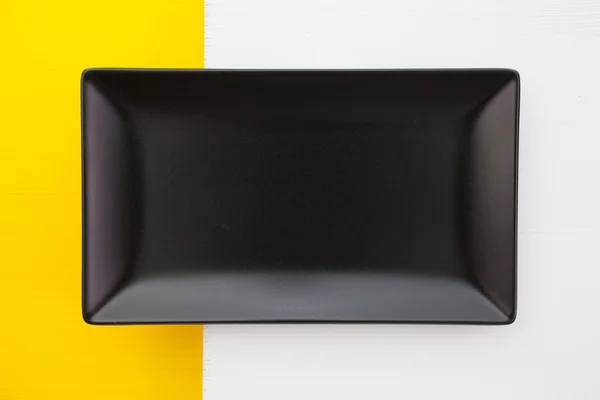 Piatto vuoto in ceramica nera su fondo bianco e giallo , — Foto Stock