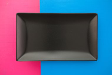 Boş siyah seramik tabak üzerinde mavi ve pembe arka plan, recta üzerinde