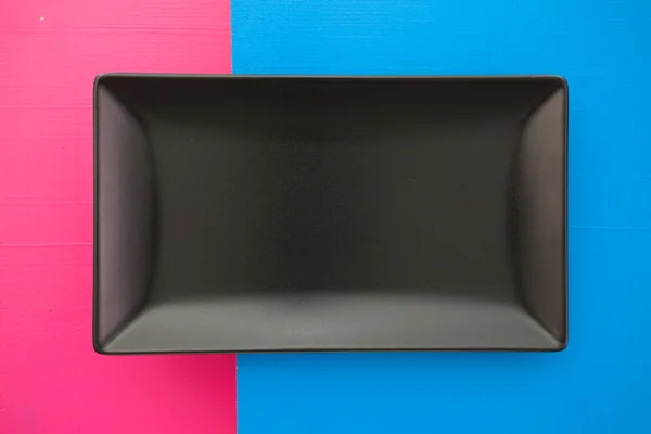 Prato de cerâmica preto vazio sobre fundo azul e rosa, recta — Fotografia de Stock