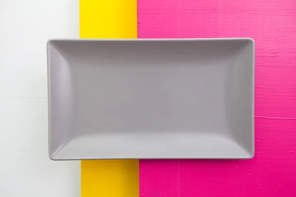 Prato de cerâmica cinza vazio sobre madeira branca, amarela e rosa — Fotografia de Stock