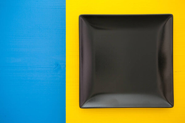Empty black ceramic dish on over blue and yellow background, 