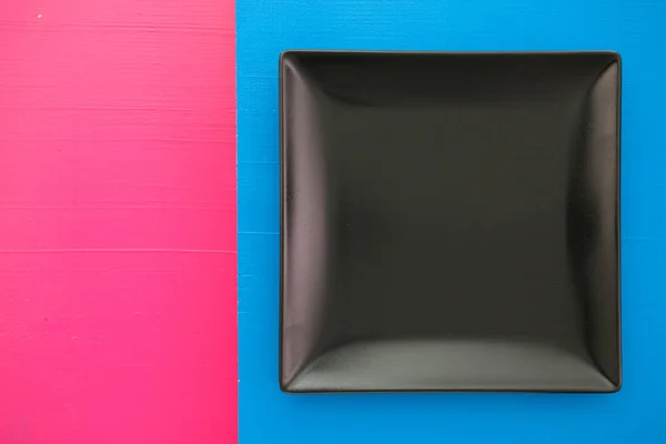 Üres fekete kerámia tányér a felső kék és rózsaszín háttér, nég — Stock Fotó