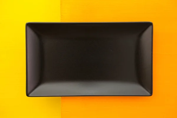 Empty black ceramic dish on over orange  and yellow wooden table — Stock Photo, Image