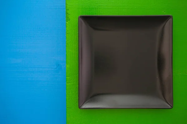 Άδειο μαύρο κεραμικό πιάτο σε πάνω από το μπλε και το πράσινο φόντο, στήριγμα τοποθέτησης — Φωτογραφία Αρχείου