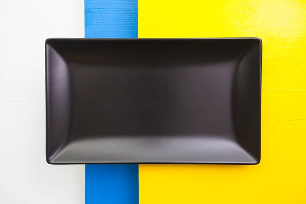 Pusty czarny naczynie ceramiczne na biały, niebieski i żółty drewniane — Zdjęcie stockowe