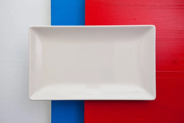 Empty white ceramic dish on over white,blue and red wooden table — Stock Photo, Image