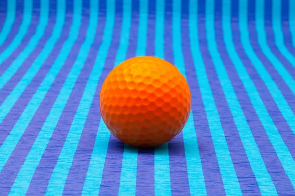 Orangefarbener Golfball auf blau gestreiftem Tisch. — Stockfoto