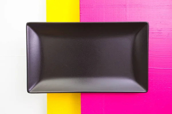 Empty black ceramic dish on over white, yellow and pink   wooden
