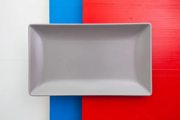 Plato de cerámica gris vacío sobre mesa de madera blanca, azul y roja — Foto de Stock