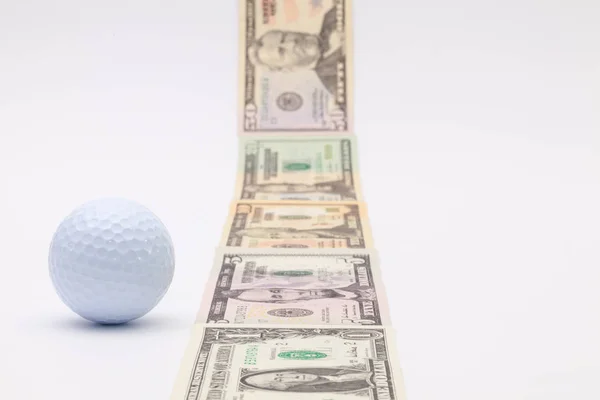 Strip of different us dollar banknotes and white golf ball — Stock Photo, Image