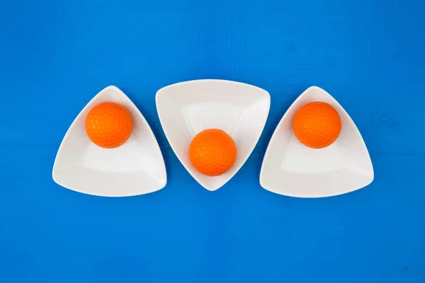 Orangefarbene Golfbälle auf den dreieckigen Keramikschalen — Stockfoto