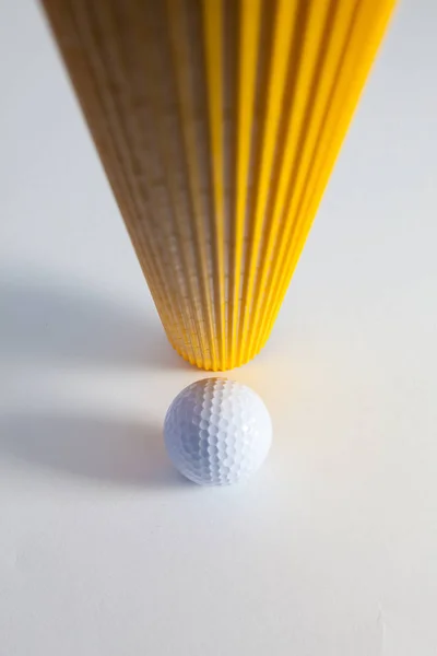Гофрированный желтый бумажный рулон и мячик для гольфа на белом столе . — стоковое фото