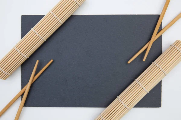 Placa rectangular de pizarra con palillos, estera de bambú para sushi o — Foto de Stock