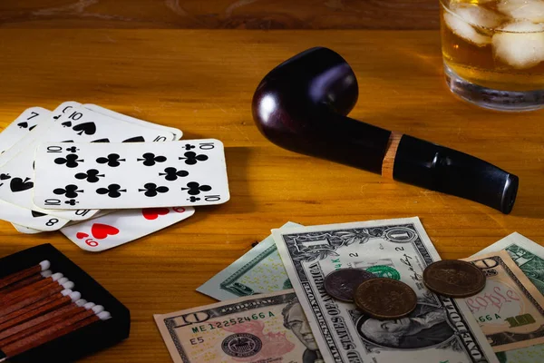 Gambling -  Smoking pipe , playing cards, Scotch whiskey and US dollars banknotes on the  wooden table