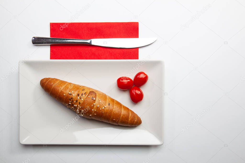 French baguette and red cherry tomatoes on the white table.