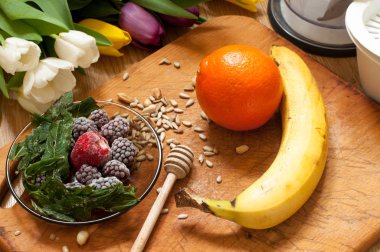 muz, portakal, dondurulmuş çilek böğürtlen ve tohum canlı smoothie maddeler ve blender, meyva suyu sıkacağı, arka planda laleler