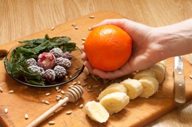 Yemek, muz, portakal, dondurulmuş çilek böğürtlen ve tohum canlı smoothie maddeler ve blender, meyva suyu sıkacağı, Lale arka planda tutan el