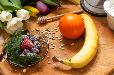 muz, portakal, dondurulmuş çilek böğürtlen ve tohum canlı smoothie maddeler ve blender, meyva suyu sıkacağı, arka planda laleler