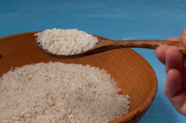 Raw rice in wooden bowl with wooden spoon on blue background