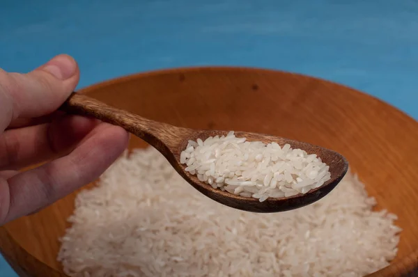 Raw rice in wooden bowl with wooden spoon on blue background