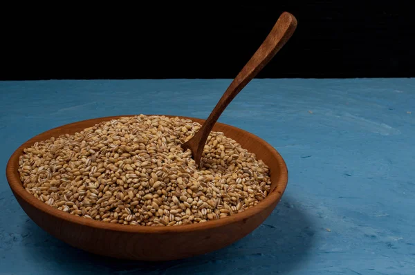 Ahşap kase pearl arpa mavi ve siyah arka plan ile. Yakın çekim.